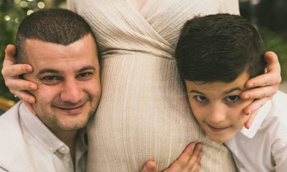 A joyful family moment with father and son embracing the pregnant mother, symbolizing love and togetherness.